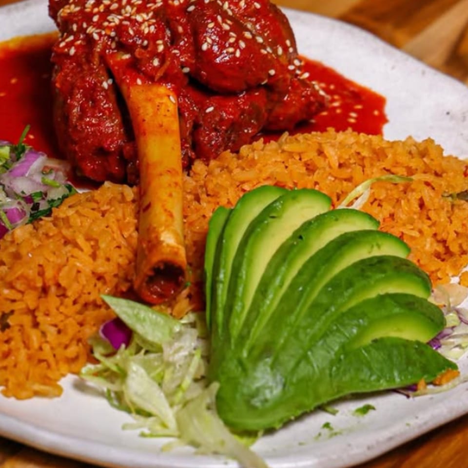 Plate of sesame-crusted red chicken, Mexican rice, avocado slices, and shredded lettuce garnish.