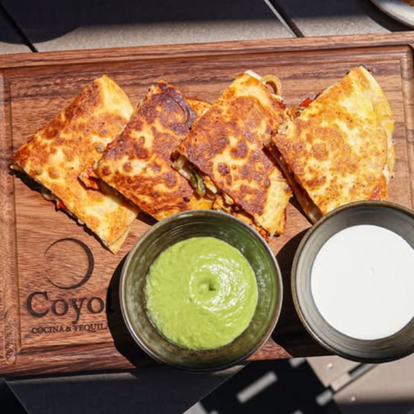 Grilled quesadilla wedges served on a wooden board with green salsa and white crema at Goyo Cocina y Tequila.